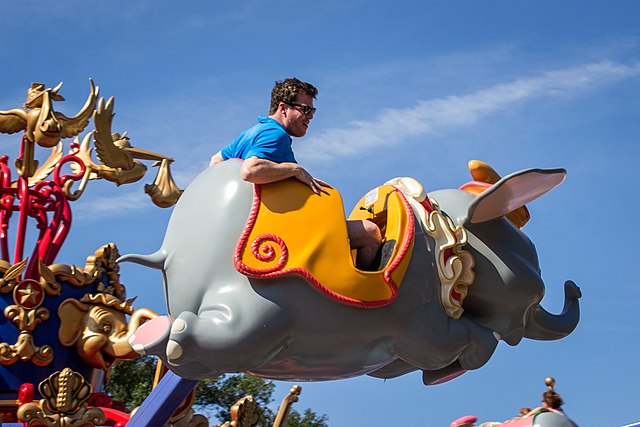 Man in blue shirt having fun riding Dumbo the Flying Elephant at Magic Kingdom