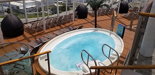 Hot Tub on the Harmony of the Seas. White Hot Tub, Light Blue Water, Surrounded by Brown Deck and Brown Lounge Chairs.