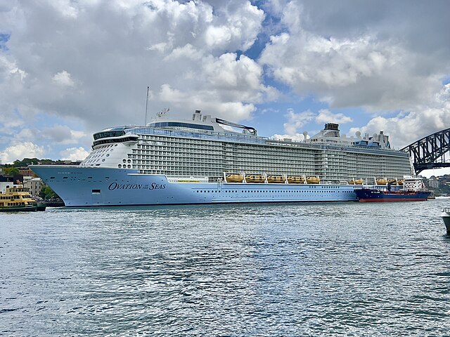 Royal Caribbean Ovation of the Seas. Large Light Blue Ship with Smaller Accompanying Ships flanking. Bridge in Background