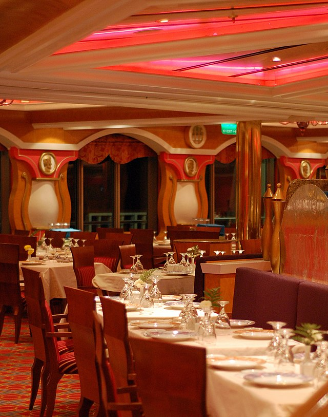 Main Dining Room on Carnival Cruises. Multiple tables with white tablecloth, empty plates, empty chairs, and upside down glasses.